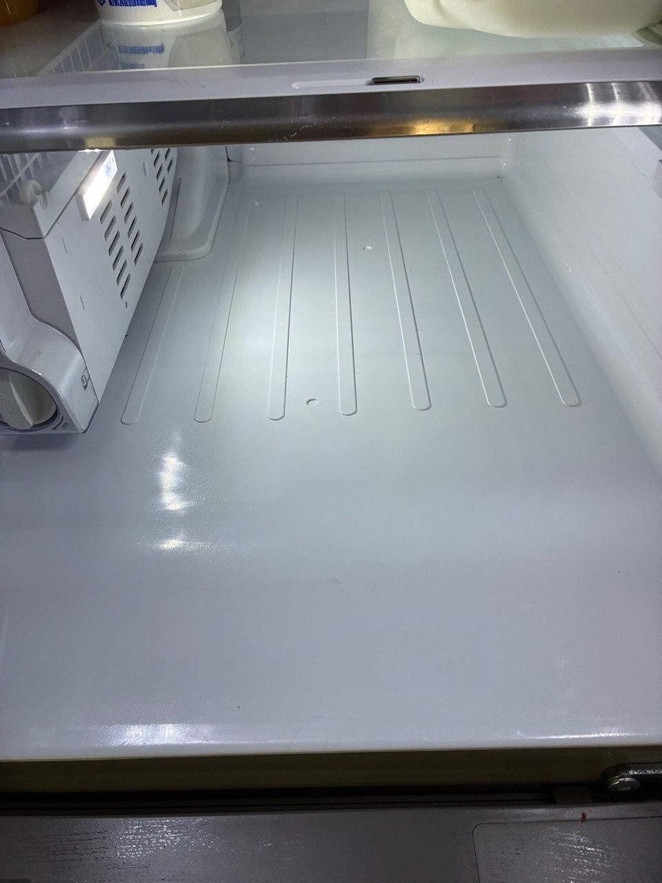 The same refrigerator shelf emptied and wiped spotless after a deep clean